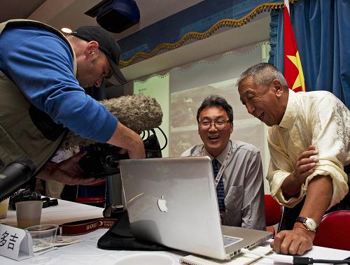 9月5日，中国藏学家代表团成员、西藏自治区文联摄影家协会主席旺久多吉（右）通过自己的笔记本电脑，向多伦多当地媒体记者展示西藏发展今昔对比图片